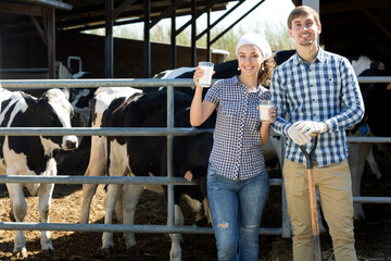 Cheerful young man and woman having glass of fresh milk on the farm