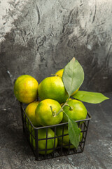 Vertical view of fresh green mandarins with leaves in a basket on gray background