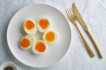 Soft-boiled eggs, peeled and cut into two halves, lying on white plate. High cholesterol, healthy Breakfast, protein food.