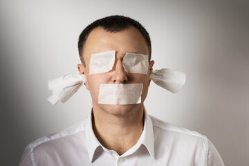 A man with eyes, mouth and ears sealed with painting tape. A concept on the topic of fear of...