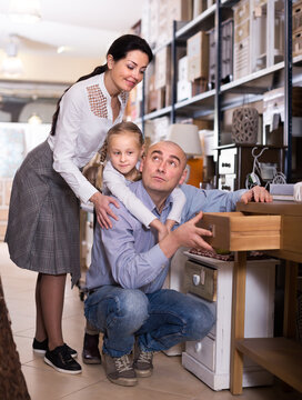 Family with small daughter are looking on new furniture in shop..