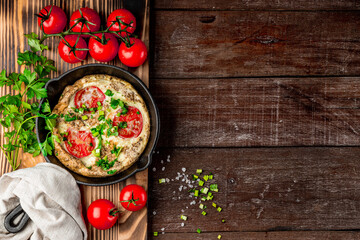  Homemade omelet with tomatoes and herbs in a pan on a wooden background with space for text, top view