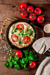  Homemade omelet with tomatoes and herbs in a pan, top view
