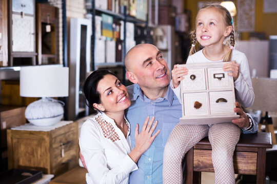 Positive couple with their daughter are demonstrating curbstone in furniture shop