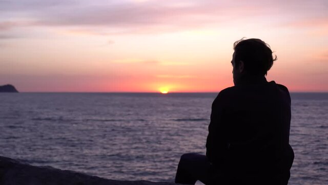 Sad young alone man looks thoughtfully at the ocean. Beautiful sunrise background. Travel and self-isolation, social distancing. Nature, sea, beach, morning