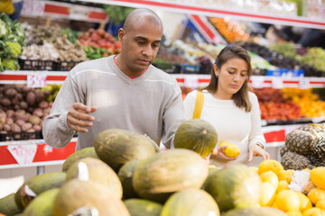 Married couple picking ripe melon at a grocery supermarket