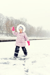 Fototapeta na wymiar cute little girl 4 years old in a pink down jacket and a hood laughs and runs along a snowy path in a snowfall
