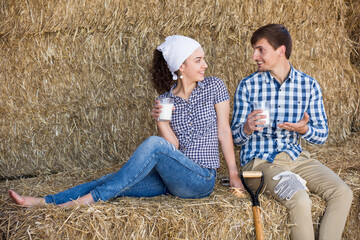 Naklejka na ściany i meble portrait of two young happy farmers taking a pause in the hay and having a glass of milk in hands