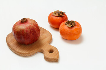 Ripe fresh pomegranate and persimmon fruits with cutting board.