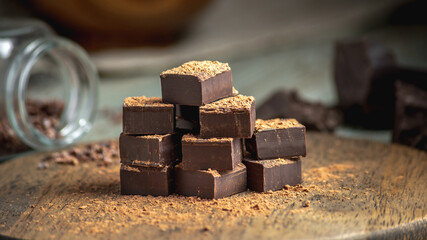 Delicious cubes of bitter dark chocolate strewed with cocoa powder on a wooden table