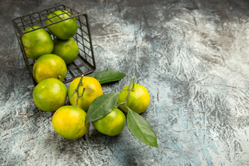 Horizontal view of fallen basket with fresh green tangerines cut in half and peeled tangerine on gray background