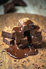 Delicious appetizing dark chocolate bars of a square shape are stacked in a tower and poured with liquid chocolate
