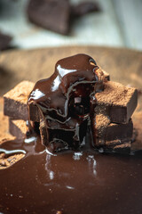 Delicious appetizing dark chocolate bars of a square shape are stacked in a tower and poured with...