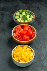 side close view of bowls of cucumber tomato and pepper on dark green background