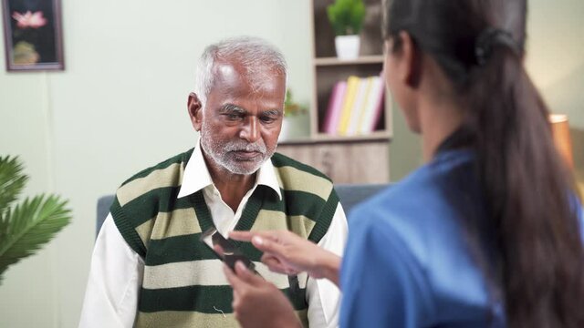 Shoulder shot of doctor explaining to patient about health details by using mobile app on phone during routine home visit