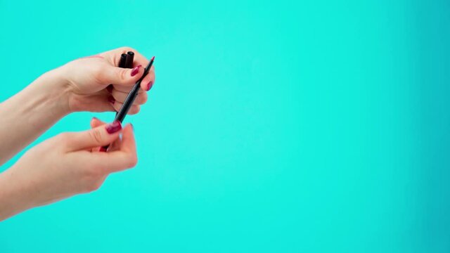Female hands holding cosmetic eye liner pencils against blue background