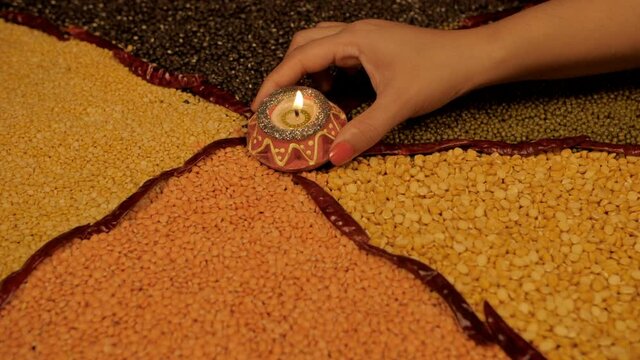 Various lentils/Dal separated by dried red chilies set on a table - protein-rich source. Female's hand keeping a decorative candle/diya in the middle of a table with legumes/pulses - Moong  Arhar  ...