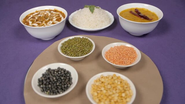Raw lentils / Dal kept on a rotating table with a cooked meal of Dal-Chawal. Closeup view of Dal Makhani and Dal Fry / Tadka served with plain steamed rice - traditional Indian cuisine