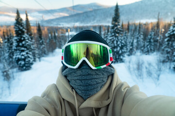Fototapeta na wymiar Young skier, snowboarder sits in a cabin at a ski resort, photographs himself, an unrecognizable face, a protective mask, a ski resort