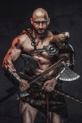 Savage and skilled scandinavian warrior with bald head wielding two axes and in armour with fur in...