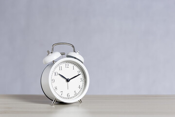 White retro analog alarm clock on table gray background with light and shadow, copy space.