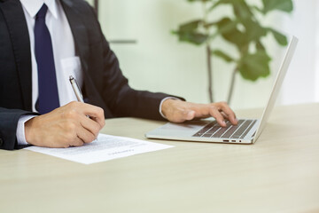 Close up hand of businessman holding pen and writting on paperwork using laptop in office. business concept.