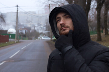 Fototapeta premium Pensive man near an empty road. A man in a hood with a pensive look.