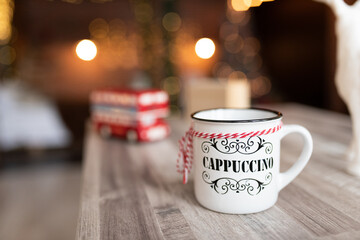 A cup of cappuccino stands on the table against the background of Christmas lights.
