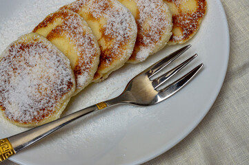 cottage cheese cakes with powdered sugar on a white plate, top view