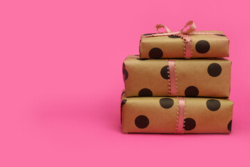 Stack of gift boxes wrapped in craft paper with ribbon bow on a pink background