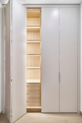 Fototapeta premium Large lobby wardrobe with LED lighting and white folding doors inner shelves and drawers made of light laminated boards in designed hallway