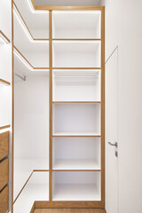 Elegant white shelving with LED lighting. Shelving of laminated boards with edges and faces of drawers made of oak veneer plywood sheets in walk-in closet