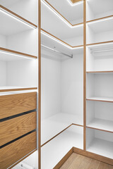 Elegant white shelving with LED lighting. Shelving of laminated boards with edges and faces of drawers made of oak veneer plywood sheets in walk-in closet
