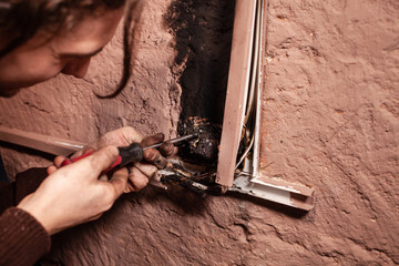 A man fixes a burnt socket. Short circuit, burnt wires. traces of smoke fire on the wall. The...