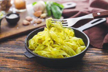 Frying pan with tasty pasta and pesto sauce on wooden table