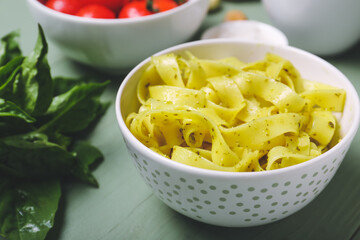 Bowl with tasty pasta and pesto sauce on color background