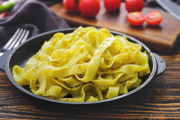 Frying pan with tasty pasta and pesto sauce on wooden table