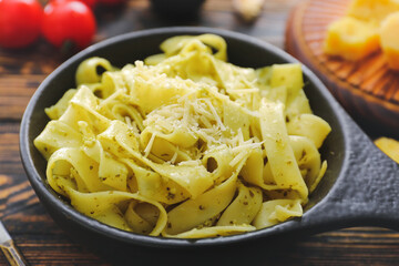 Frying pan with tasty pasta and pesto sauce on dark wooden table, closeup