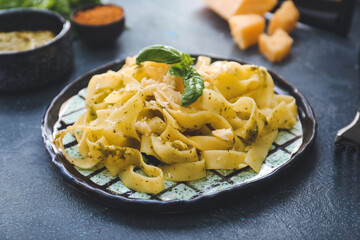 Plate with tasty pasta, pesto sauce and ingredients on dark background