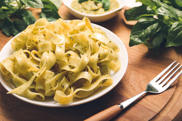 Wooden board with tasty pasta, pesto sauce and green basil on table