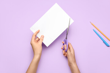 Woman cutting paper with scissors on color background