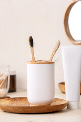 Holder with wooden toothbrushes and toothpaste on table in bathroom