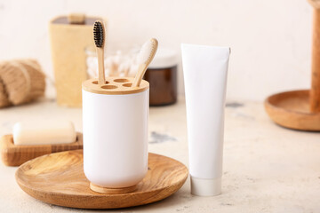 Holder with wooden toothbrushes and toothpaste on table in bathroom