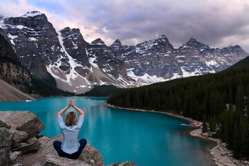 Woman meditating on cliff above turquoise mountain lake. Moraine Lake in Banff National Park....