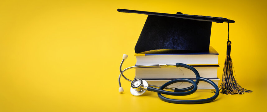 medical education - college graduation cap with stethoscope and books on yellow background with copy space