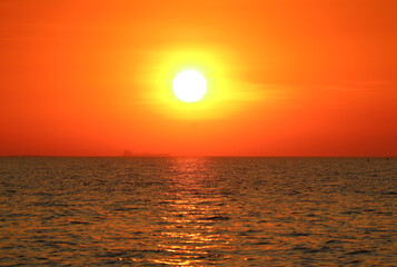 Bright sun on the vivid orange sky setting over the calm sea