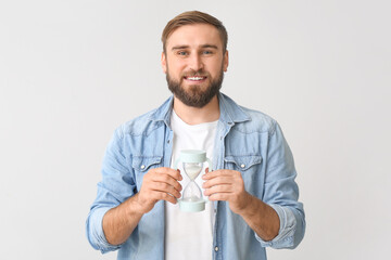 Young man with hourglass on light background