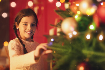 Obraz na płótnie Canvas Cute little girl decorating Christmas tree at home