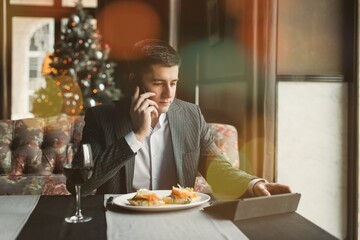 A young and attractive man uses his phone while delicious eggs benedict with lightly salted salmon and sauce in an indoor restaurant