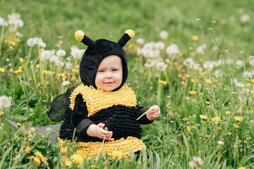 cute and cheerful portrait of little child sitting in blooming flowers of dandelion in yellow bee...
